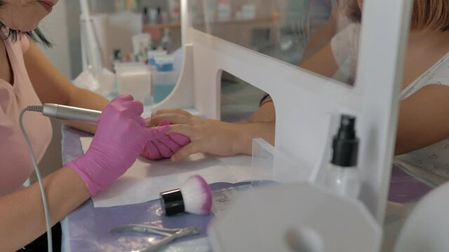 esmaltado de u&ntilde;as u manicura en cl&iacute;nica de belleza en mano de ni&ntilde;a por esteticista con guantes rosas
