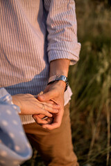 Couple hold hands in green field on sunset. Close up.