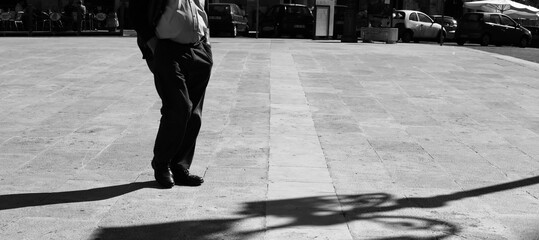 Sicilian man in a square with his hands in his pockets with elongated shadow in black and...