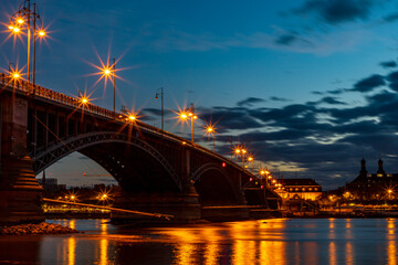 Fototapeta na wymiar The illuminated Theodor Heuss Bridge that crosses the Rhine between Mainz and Wiesbaden at night. In the background the silhouette of Mainz