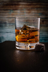 A glass of Kentucky Bourbon on rocks and chocolate candy  placed on black stone with colored wooden background