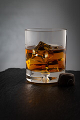 Glass of Kentucky bourbon whiskey with chocolate candy next to it reflecting on black stone surface