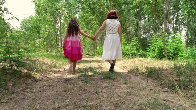 Dos ni&ntilde;as hermanas cogidas de la mano pasean por camino de bosque y un dron las sigue de espalda