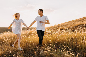 Young romantic couple running in an open field with dry grass, holding hands.