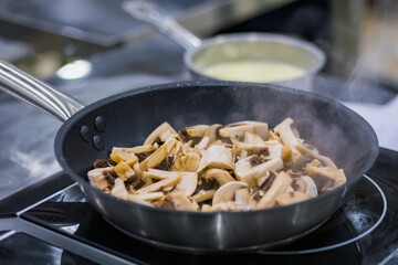 Process of cooking sliced champignon mushrooms in black frying pan with oil on electric stove. Professional cooking, catering, cookery, gastronomy and food concept
