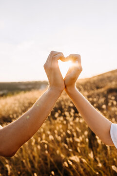 Hands of a couple making a heart shape in a field.