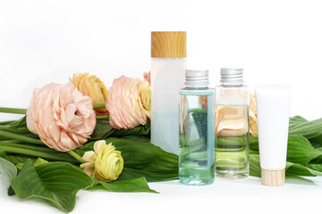 Reusable bottles with liquid on yellow pink ranunculus flowers and green leaves background