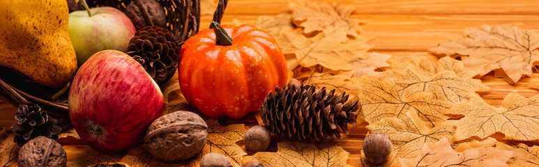 Autumnal decoration and food scattered from wicker basket on golden foliage on wooden background,...