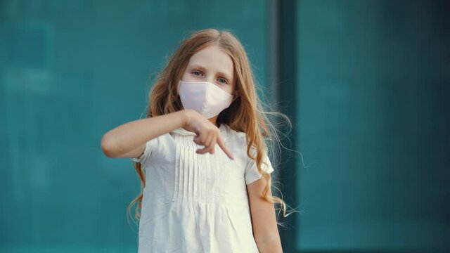 Small active positive girl not afraid of infection with respiratory virus, wears protective fashionable medical mask on face, dances in empty city in quarantine, moves her arms, makes wave with hands