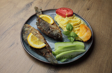 Fried fish and vegetables on a plate. On a wooden table