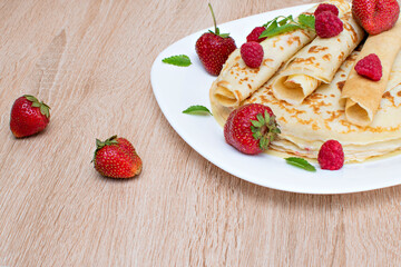Pancakes with strawberries and raspberries. Pancakes with raspberries and strawberries on a plate. Pancakes with raspberries and strawberries on a plate and a wooden board.