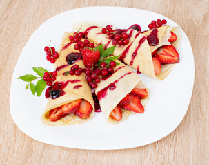 Pancakes with cranberries and strawberries on a plate. Pancakes with berries, strawberries and chocolate syrup. Breakfast with pancakes with strawberries and berries on a plate..