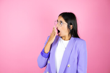 Young beautiful business woman over isolated pink background with her hand over her mouth and surprised, looking side