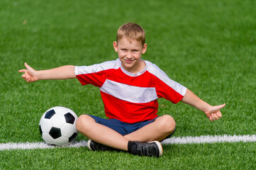 Boy posing with soccer ball on green grass. Sports training in the field. Kid sport online concept