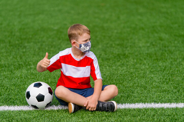 School kid with mask and soccer ball in a physical education lesson. Safe back to school during pandemic concept. Social distancing to fight COVID-19