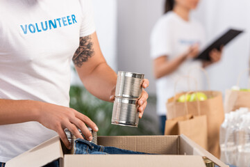Cropped view of volunteer putting tin cans in carton box
