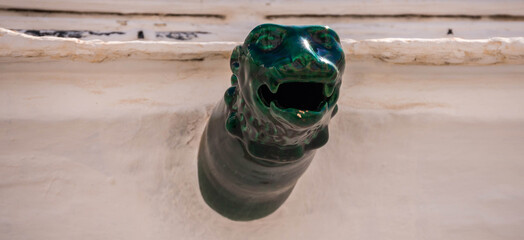 Ceramic green gargoyle on a white wall, an interesting traditional architectural element