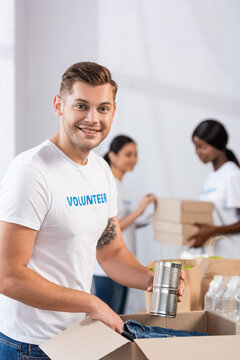 Selective focus of volunteer holding tin cans near package in charity center