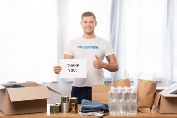 Volunteer showing like while holding card with thank you lettering near donations on table