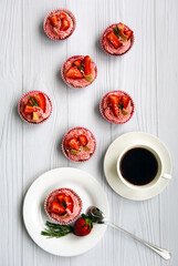 Appetizing pink cupcakes with strawberries and cream on a white plate and a light wooden background