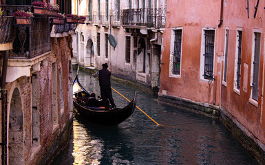 Fototapeta na wymiar Venice, Italy. Curved gondola in a narrow canal in the middle of ancient houses with brick-colored walls. Atmosphere of peace and serenity.