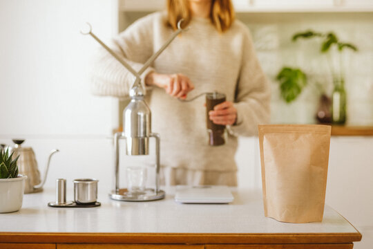 Woman grinding coffee near coffee machine at home.