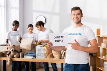 Selective focus of volunteer pointing at card with donate today lettering in charity center