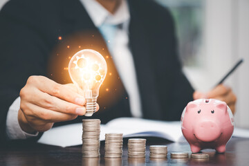 Businessman hand holding light bulb with line connect and Coins stack on the wooden table , Saving...