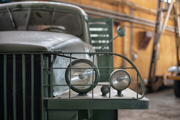 Fragment of an old green truck in the garage with a focus on the headlights with a metal grille