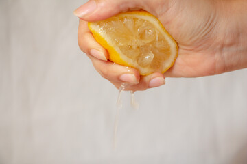 Close up female hand squeezing half of lemon on white background.