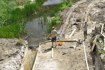 Repair of the dam on the river. Two workers are building the formwork.