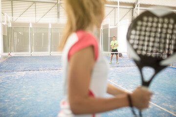 paddle tennis indoors training, woman serving ball, focus on man