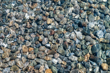 Texture of multicolored pebbles in a clear shallow sea water