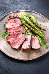 Barbecue dry aged wagyu roast beef steak with green asparagus and lettuce offered as close-up on a rustic modern design plate