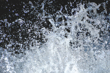 Fototapeta na wymiar Closeup of sparkling drops of water splashing up from rushing stream captured and frozen in midair. Attention-grabbing image of tiny water droplets isolated against dark background.