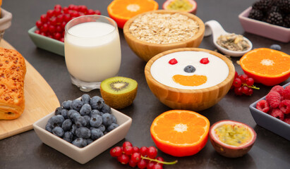 Breakfast Served in the morning with Butter bread and corn flakes Whole grains and raisins with milk in cups and Strawberry, Blueberry, Raspberry, Kiwi, Fresh Orange  on the breakfast table.