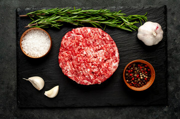 Raw beef burger cutlets with rosemary and spices on a slate board on a concrete background