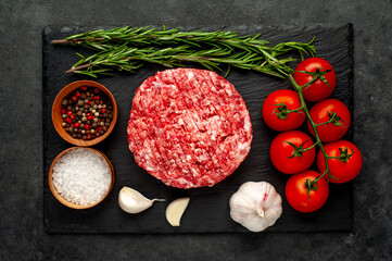 Raw beef burger cutlets with rosemary and spices on a slate board on a concrete background