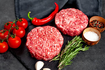 Raw beef burger cutlets with rosemary and spices on a slate board on a concrete background
