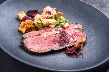 Modern style Commonwealth Sunday roast with sliced cold cuts roast beef, pickled mushrooms and vegetable chips offered as close-up on a cast-iron design plate