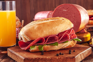 Mortadella sandwich with orange juice and piece of mortadella on wood background