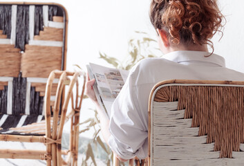 Tiempo de relajarse y leer. Mujer adulta leyendo una revista de espaldas cómodamente sentada y relajada dentro de una habitación cálida e iluminada en un apartamento confortable y moderno. 