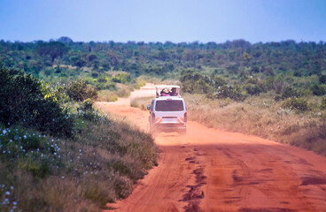 Obraz na płótnie Canvas The car is driving on a dirt road in Tsavo National Park East Kenya. People are on a safari trip in nature.