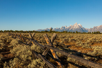 Split rail fence with morning frost runs across a sage covered meadow in front of the Teton mountains in Grand Teton National Park