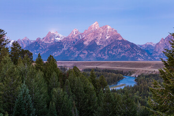 Pink light of dawn shines across the Teton mountains and the Snake River as seen from the Snake...