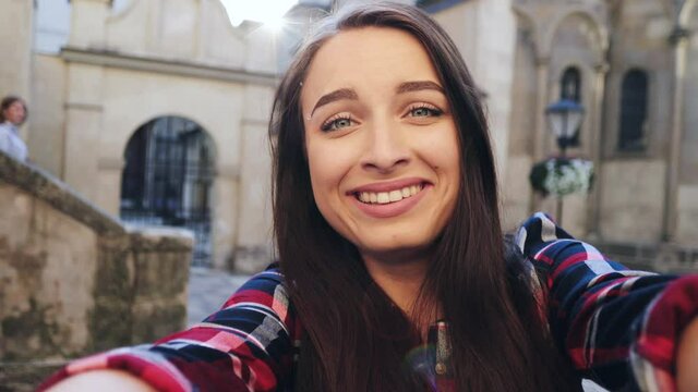 Close up portrait of attractive girl with brown hair in plaid shirt. Cheerful girl grimaces at the camera while standing outside. Camera view.