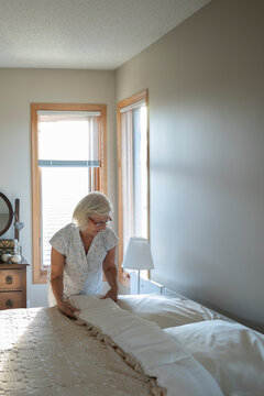 Senior woman making bed in morning bedroom