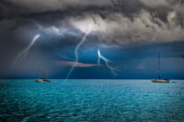 Yachts are at sea in a storm. Lightning flashes from the sky into the water. It's in Sardinia,...