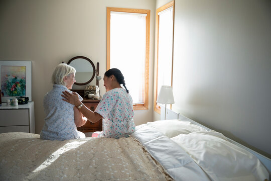 Home caregiver comforting senior woman in bedroom