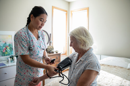 Home caregiver taking blood pressure of senior woman in bedroom